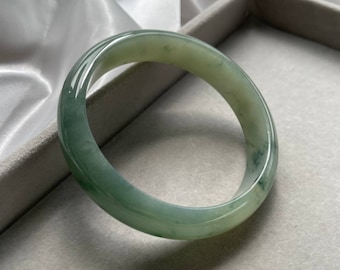 May include: A light green jade bangle bracelet. The bangle is smooth and polished, with a slightly oval shape.