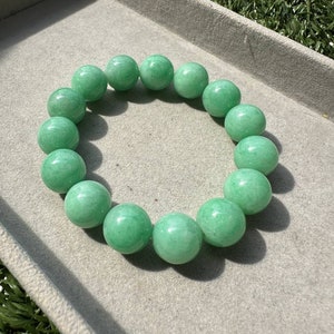 K&ouml;nnte beinhalten: Ein gr&uuml;nes Jadearmband mit runden Perlen. Das Armband ist aus nat&uuml;rlichem Jade gefertigt und hat eine glatte, polierte Oberfl&auml;che.