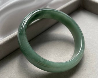 May include: A green jade bangle bracelet. The bangle is smooth and polished, with a light green color.