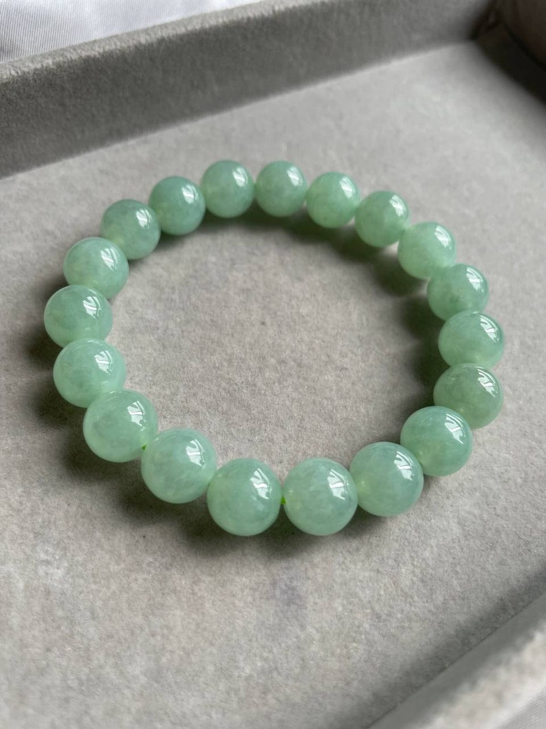 May include: A jade green beaded bracelet with round beads. The bracelet is made of natural jade and has a smooth, polished finish.