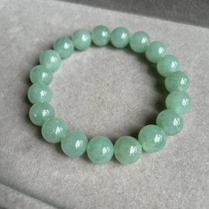 May include: A jade green beaded bracelet with round beads. The bracelet is on a light gray surface.
