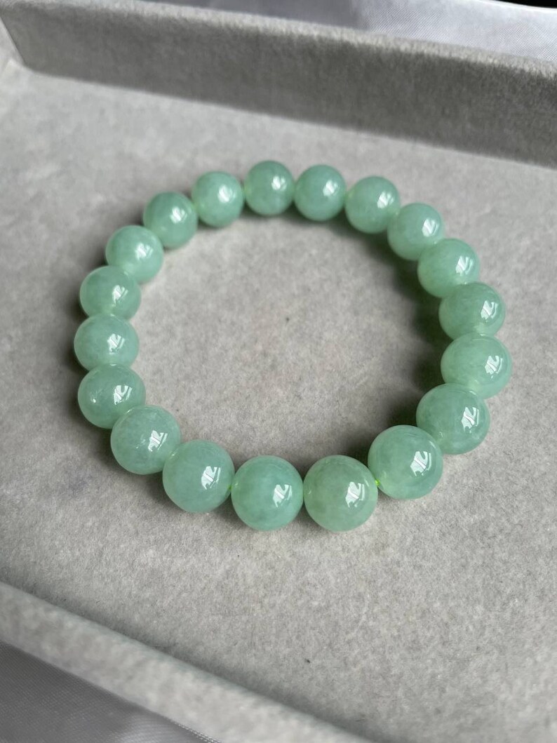May include: A jade green beaded bracelet with round beads. The bracelet is on a light gray surface.