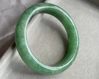 May include: A green jade bangle bracelet. The bracelet is smooth and polished, with a light green color.
