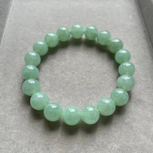 May include: A jade green beaded bracelet with round beads. The bracelet is made of natural jade and has a smooth, polished finish.