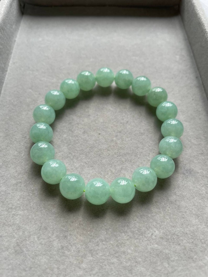 May include: A jade green beaded bracelet with round beads. The bracelet is made of natural jade and has a smooth, polished finish.