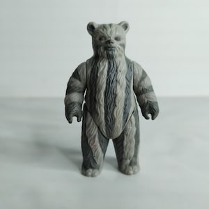 Puede incluir: Una figura de acción de peluche gris y blanco de un personaje de Star Wars, un Wookiee, con una barba larga y un patrón a rayas en su cuerpo.