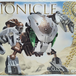 Puede incluir: Figura Bionicle Pahrak-Kal. La figura es principalmente plateada, marrón y verde, con un diseño estampado en la cabeza. La imagen incluye el logotipo de Lego y el número 8577. El fondo es una escena desértica.