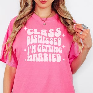 May include: A pink t-shirt with white text that reads 'Class Dismissed I'm Getting Married' in a retro font.