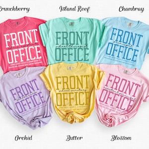 May include: Six colorful t-shirts with the words "FRONT OFFICE" printed on them. Each shirt has a different title below the words "FRONT OFFICE", such as "admin assistant" or "school therapist". The shirts are in various colors, including pink, blue, and yellow.