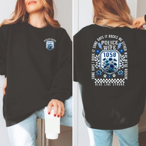 May include: Black sweatshirt with a blue and white graphic on the back that says "Some days I rock it some days it rocks me either way we're rockin' Police Wife 1058 Blue Line Strong". The front of the sweatshirt has a blue and white graphic that says "Police Wife James".