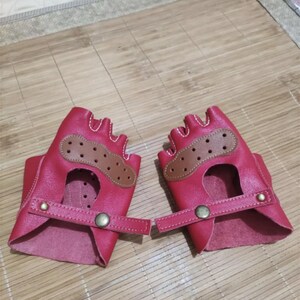 May include: A pair of red leather fingerless gloves with brown leather accents and a snap closure. The gloves have a perforated design and are made of a soft, supple leather.