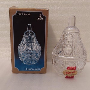 May include: A clear glass pear-shaped candy dish with a lid. The dish is made of lead crystal and has a hand-cut design. The box says "Fait à la main" and "Crystal au plomb".