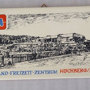 Peut inclure: Une illustration en noir et blanc d'un bâtiment avec le texte "Mainland-Freizeit-Zentrum Hochberg/Bayern". L'illustration est sur un fond blanc avec un logo "M" bleu et rouge dans le coin supérieur gauche.