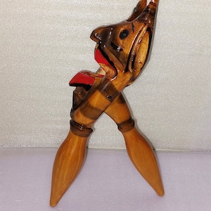 Op de afbeelding: Een houten notenkraker in de vorm van een gezicht met een rood geverfde mond. De notenkraker is geschilderd met bruine en zwarte strepen en heeft een gedetailleerd gesneden ontwerp.