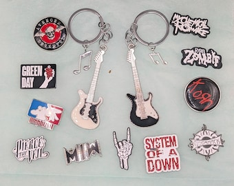 May include: Two silver-toned electric guitar keychains with music note charms, surrounded by various band logo enamel pins including Avenged Sevenfold, Green Day, Limp Bizkit, Pierce the Veil, Motionless In White, My Chemical Romance, Rob Zombie, Korn, System of a Down, Godsmack, and a skeleton hand gesture pin.