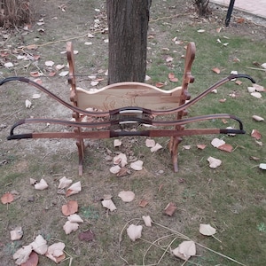 Könnte beinhalten: Drei Holzbögen mit schwarzer Sehne und braunen Ledergriffen werden auf einem Holzständer ausgestellt. Die Bögen sind versetzt angeordnet, wobei der oberste Bogen der längste und der unterste Bogen der kürzeste ist.