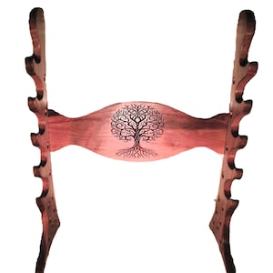 Puede incluir: Un soporte de madera para espadas con un diseño de árbol de la vida. El soporte tiene 6 ranuras para espadas y está hecho de madera marrón oscura.