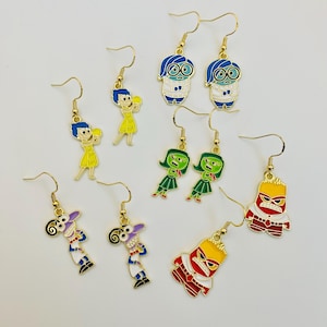 May include: A set of eight gold-tone earrings featuring characters from the animated film Inside Out. The earrings feature Joy, Sadness, Anger, Fear, and Disgust. Each earring is approximately 1 inch in length.