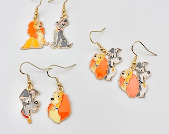 May include: Gold-tone dangle earrings featuring cartoon dog designs. The earrings showcase colorful enamel details of dogs in various poses. The designs include a yellow and orange dog, a gray dog, and a pair of dogs in orange and gray.