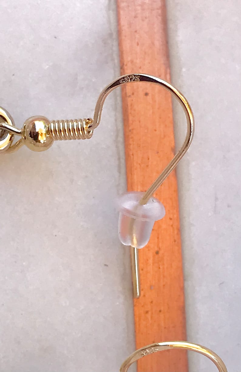 May include: Gold earring with a spring clasp and a clear plastic stopper. The earring is marked with the number "925".