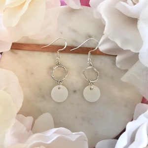 May include: A pair of silver earrings with a small white circle pendant hanging from a silver circle.