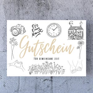 May include: A white gift certificate with black illustrations of a camera, clock, house, flowers, and hands. The text "Enjoy Every Moment" and "Gutschein für gemeinsame Zeit" is printed on the certificate.