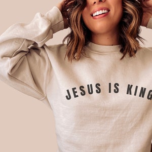 May include: A beige sweatshirt with the text "JESUS IS KING" printed in black.
