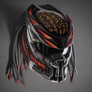 May include: A full-face motorcycle helmet featuring a dark metallic finish with vibrant orange accents and intricate glowing orange symbols on the top. The helmet includes long, braided black hair-like strands and a sculpted, textured face mask.
