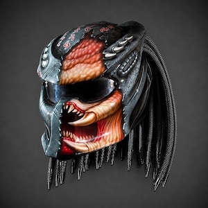 May include: A full-face motorcycle helmet featuring a custom airbrushed design of a creature with a metallic grey armoured exterior, a textured orange and tan organic face, sharp white fangs, a dark visor, and long black braided hair strands.