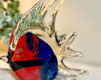May include: A clear glass sculpture shaped like an angelfish with a vibrant red and deep blue body, featuring a prominent black horizontal stripe across the center and a tall, translucent dorsal fin that tapers to a point at the top.