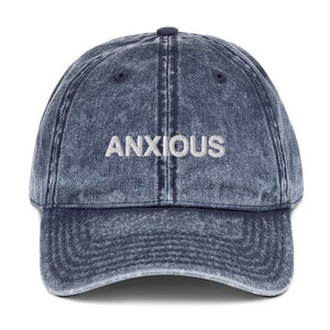 May include: A blue denim baseball cap with the word "ANXIOUS" embroidered in white on the front.