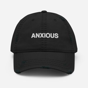 May include: Black distressed baseball cap with the word "ANXIOUS" embroidered in white. The cap features a curved peak and a worn, vintage appearance.