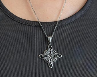 May include: A silver-colored pendant necklace featuring a Celtic knot design. The pendant is a four-pointed cross shape with intricate knotwork. The necklace is worn against a black top.