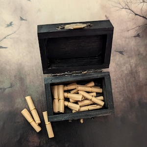 May include: A small, open, black wooden box filled with rolled-up paper scrolls. Several scrolls are outside the box. Each scroll is secured with a thin gold-colored band. The box has a brass clasp and hinges.