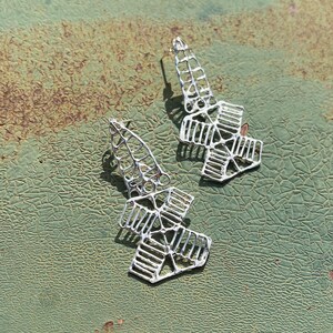 May include: A pair of silver geometric earrings with a delicate, intricate design. The earrings are made of thin metal and have a slightly curved shape.
