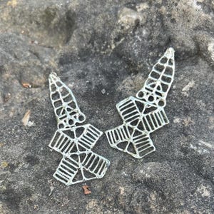May include: A pair of silver earrings with a geometric design. The earrings are made of metal and have a delicate, intricate pattern.