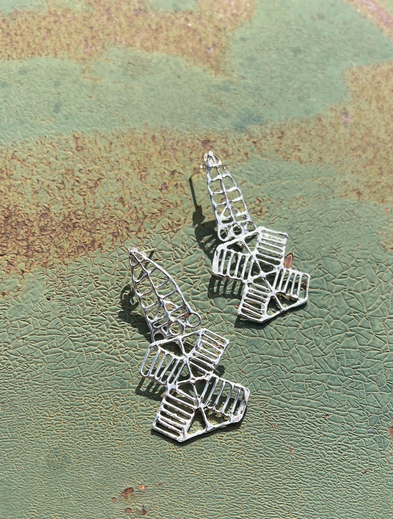 May include: A pair of silver geometric earrings with a delicate, intricate design. The earrings are made of thin metal and have a slightly curved shape.