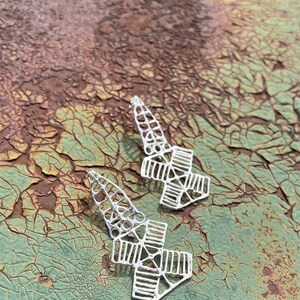 May include: A pair of silver earrings with a geometric design. The earrings are made of intricate, openwork metal and have a pointed shape.