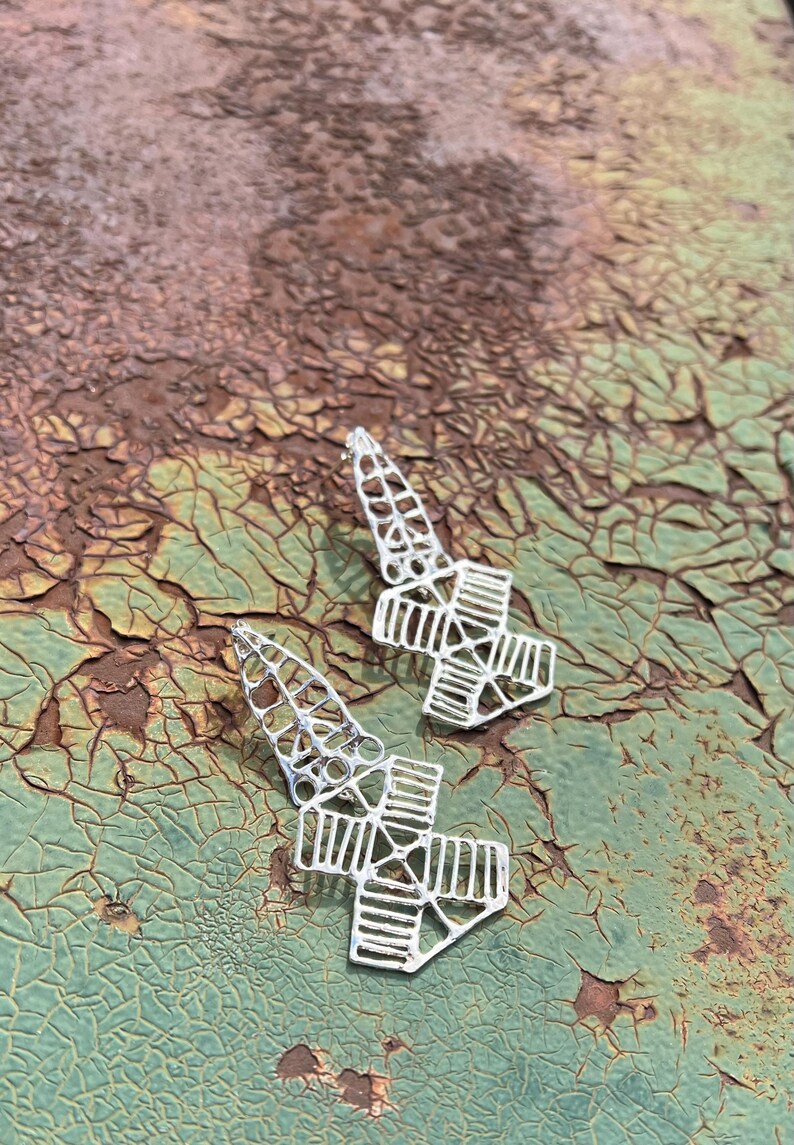 May include: A pair of silver earrings with a geometric design. The earrings are made of intricate, openwork metal and have a pointed shape.
