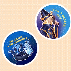 Pode incluir: Dois adesivos redondos com ilustrações de fantasia. Um apresenta um personagem com um chapéu de mago segurando uma arma, com o texto "I AM A HEALER, BUT...". O outro apresenta um personagem azul e branco com o texto "SO SHINY SO STRONG".