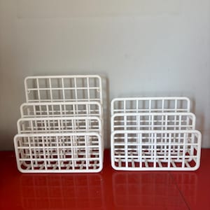 May include: Two white metal magazine racks, one with three tiers and one with two tiers, on a red surface.