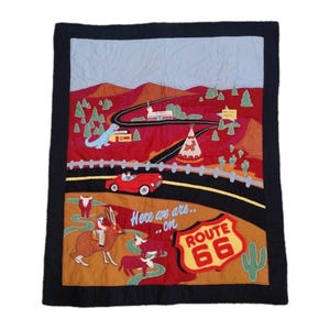 Könnte beinhalten: Gesteppte Wandbehänge mit einem Route 66-Design. Das Kunstwerk zeigt ein rotes Auto, ein Tipi, einen Dinosaurier und eine Straße, die sich durch eine Landschaft schlängelt. Die Worte "Here we are...on Route 66" sind ebenfalls sichtbar.