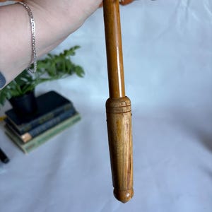 Puede incluir: Un parasol de estilo vintage con un mango de madera y una capota naranja decorativa. El mango es de color marr&oacute;n claro y la capota tiene un patr&oacute;n detallado. El parasol est&aacute; sostenido por una persona.