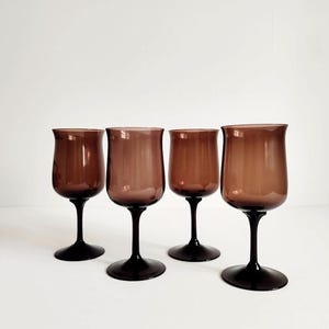 May include: Four brown wine glasses with a rounded bowl and a black stem and base. The glasses are arranged in a row against a white background. The glasses have a vintage aesthetic.