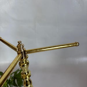 May include: A gold-colored metal decorative stand with a marble base. The stand has a three-arm design, with each arm extending horizontally. The stand is ornate, with a detailed, decorative column.