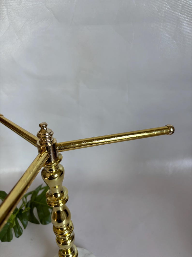 May include: A gold-colored metal decorative stand with a marble base. The stand has a three-arm design, with each arm extending horizontally. The stand is ornate, with a detailed, decorative column.
