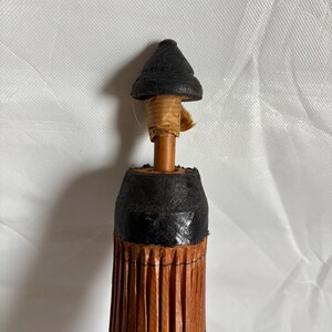 Puede incluir: Un peque&ntilde;o parasol decorativo con una parte superior negra y un cuerpo plisado marr&oacute;n. El mango es una clavija de madera fina envuelta en papel beige. El cuerpo del parasol tiene un dise&ntilde;o floral negro.