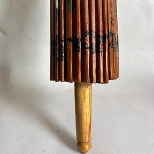 Puede incluir: Primer plano de un parasol japon&eacute;s tradicional. El parasol est&aacute; hecho de papel marr&oacute;n con dise&ntilde;os florales negros y verdes. El mango es de madera clara.