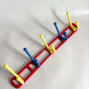 May include: A red wall-mounted coat rack with six hooks. The hooks alternate between yellow and blue, and the rack has a rectangular design. The hooks are evenly spaced along the red frame.