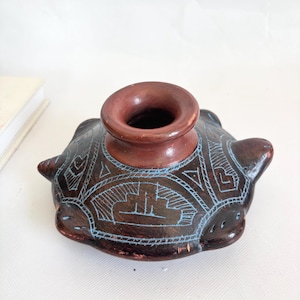 Może przedstawiać: Brązowy ceramiczny wazon z szeroką, zaokrągloną podstawą i wąską, cylindryczną szyjką. Wazon posiada skomplikowane geometryczne wzory w kolorze jasnoniebieskim i ma około 13 cm średnicy i 10 cm wysokości. Wazon ma rustykalny, ręcznie robiony wygląd.